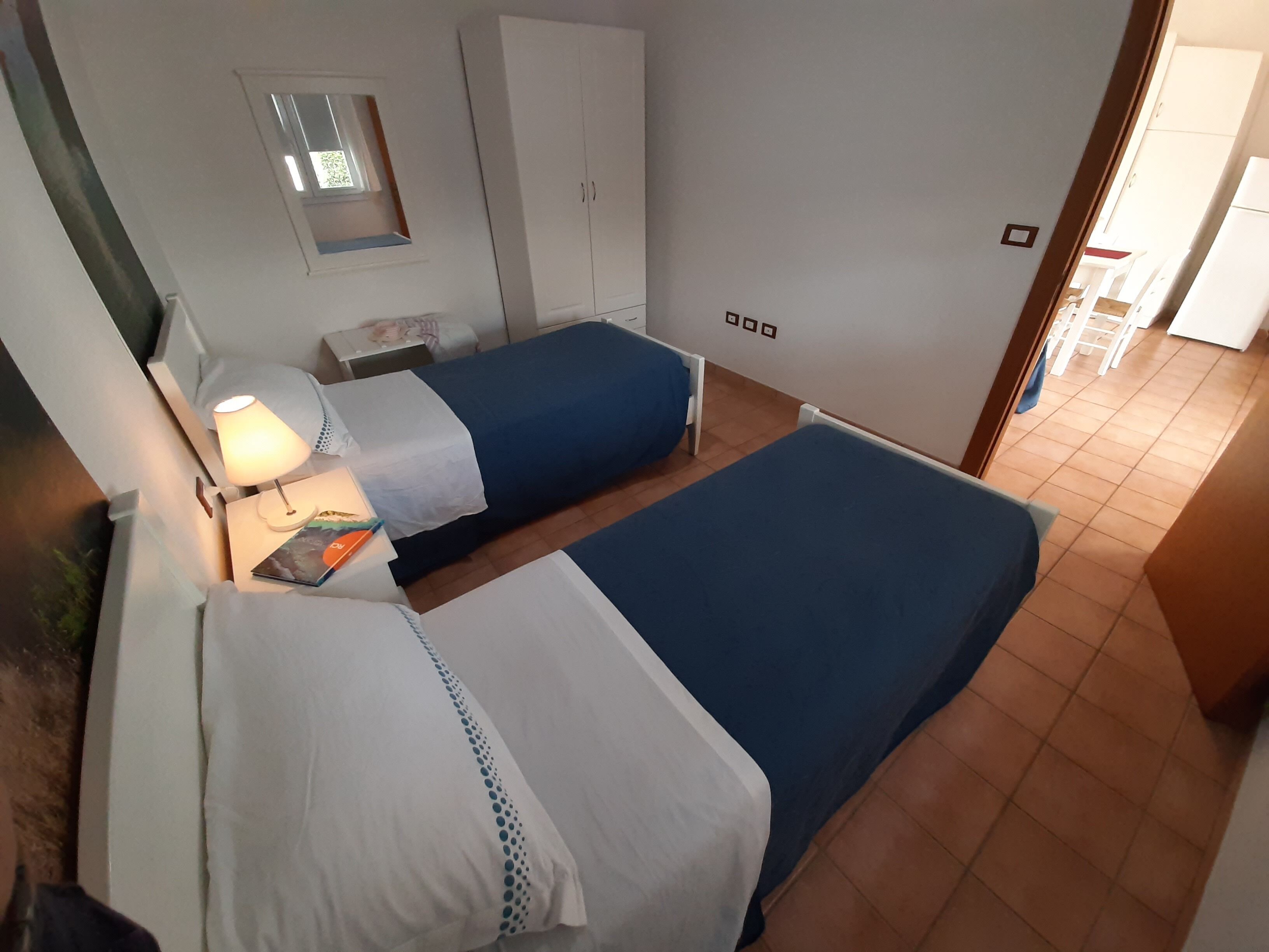 Ein Hotelzimmer mit zwei Betten, einem Schreibtisch, einem Stuhl, einer Lampe, einem Kleiderschrank und einem Spiegel.