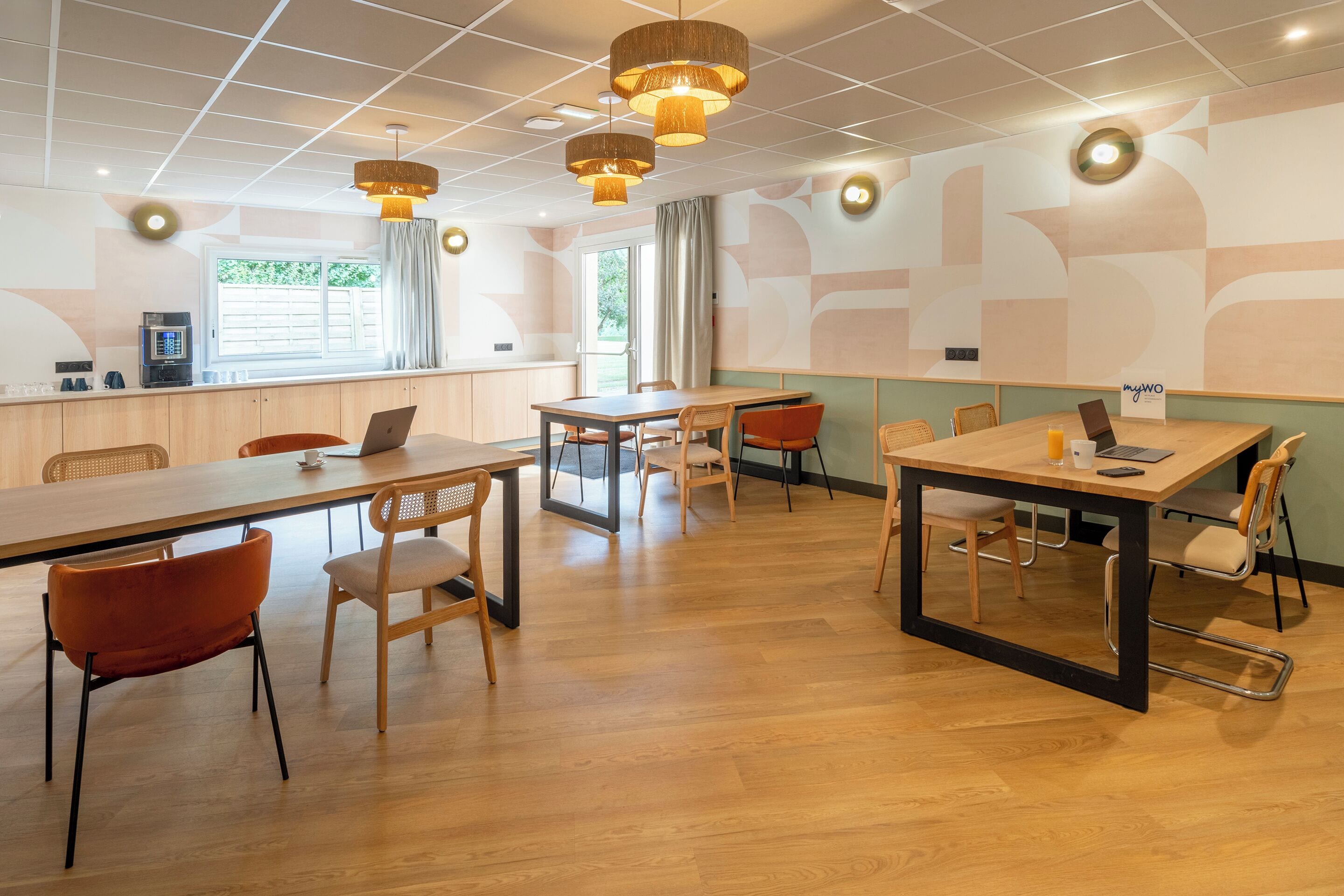A modern meeting room with wooden tables and chairs, pendant lighting, and a large window with curtains.