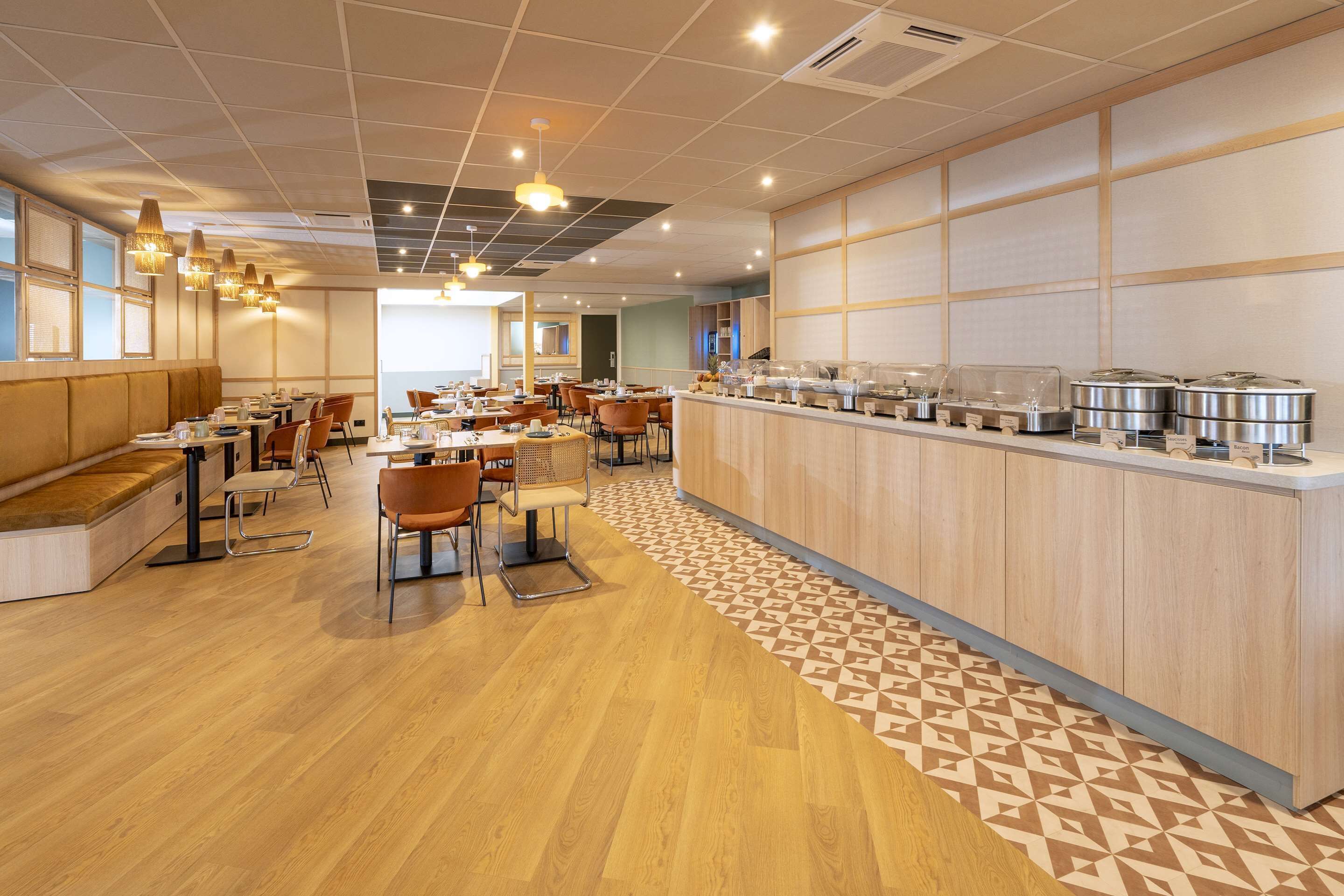 A modern dining area with wooden flooring, a central island with food dispensers, and a seating arrangement of tables and chairs.