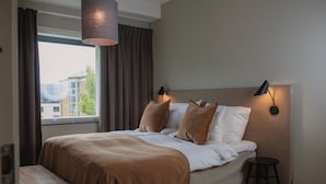 Ein ordentlich bezogenes Bett mit einer braunen Decke, eine kleine Holzbank und zwei Wandleuchten.