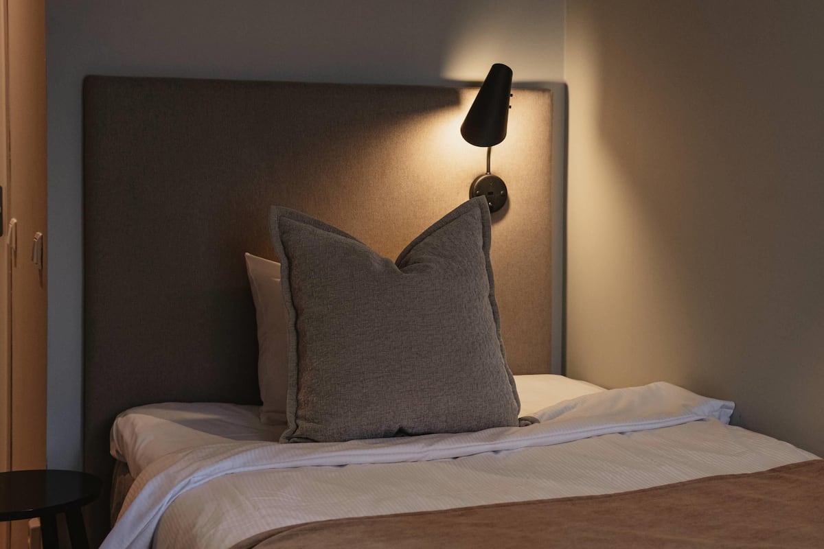 A bed with a headboard, a bedside lamp, and a pillow.