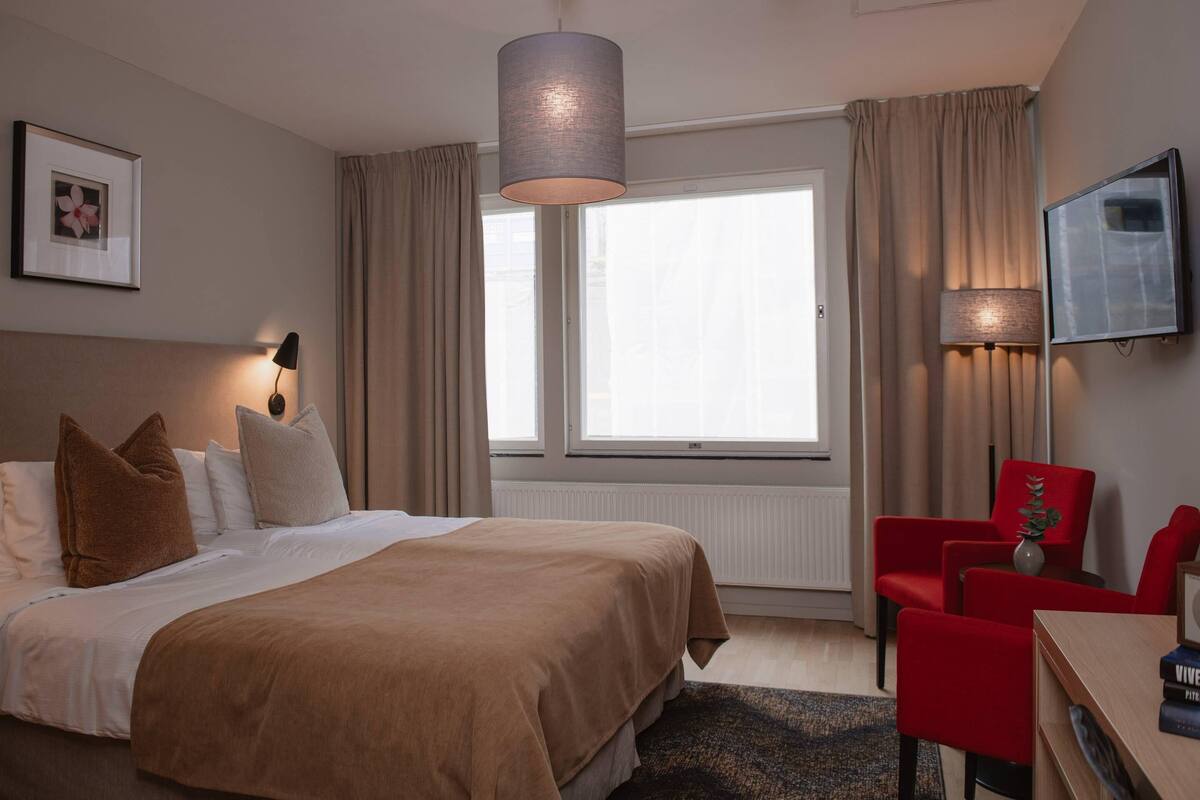 A hotel room with a bed, a desk, a chair, a television, and a window with curtains.