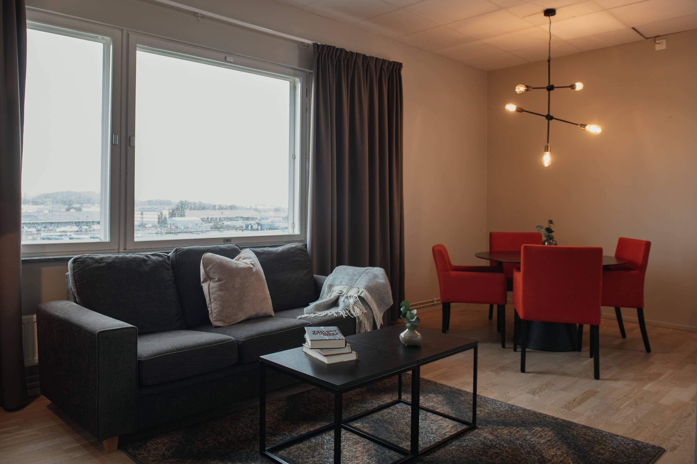 A modern living room with a sofa, coffee table, and dining area with red chairs.