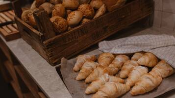 Una caja de madera llena de productos horneados variados, incluyendo pan y cruasanes, sobre una encimera de cocina.