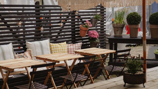 A wooden outdoor seating area with tables and chairs, a black metal fence, and potted plants. - Home Hotel Odin (Gothenburg)