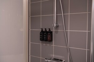 A bathroom with a tiled wall, a showerhead, and three bottles of toiletries.