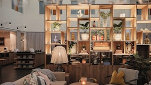 Eine moderne Hotelhalle mit einem Holzbüro, einer Sitzecke mit rundem Tisch und Stühlen sowie einem Bücherregal mit Büchern und Dekoration.