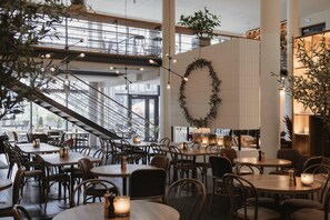 Un espace de restauration intérieur moderne, doté de plusieurs tables et chaises, d’un escalier et d’un mur décoratif orné d’un motif circulaire.