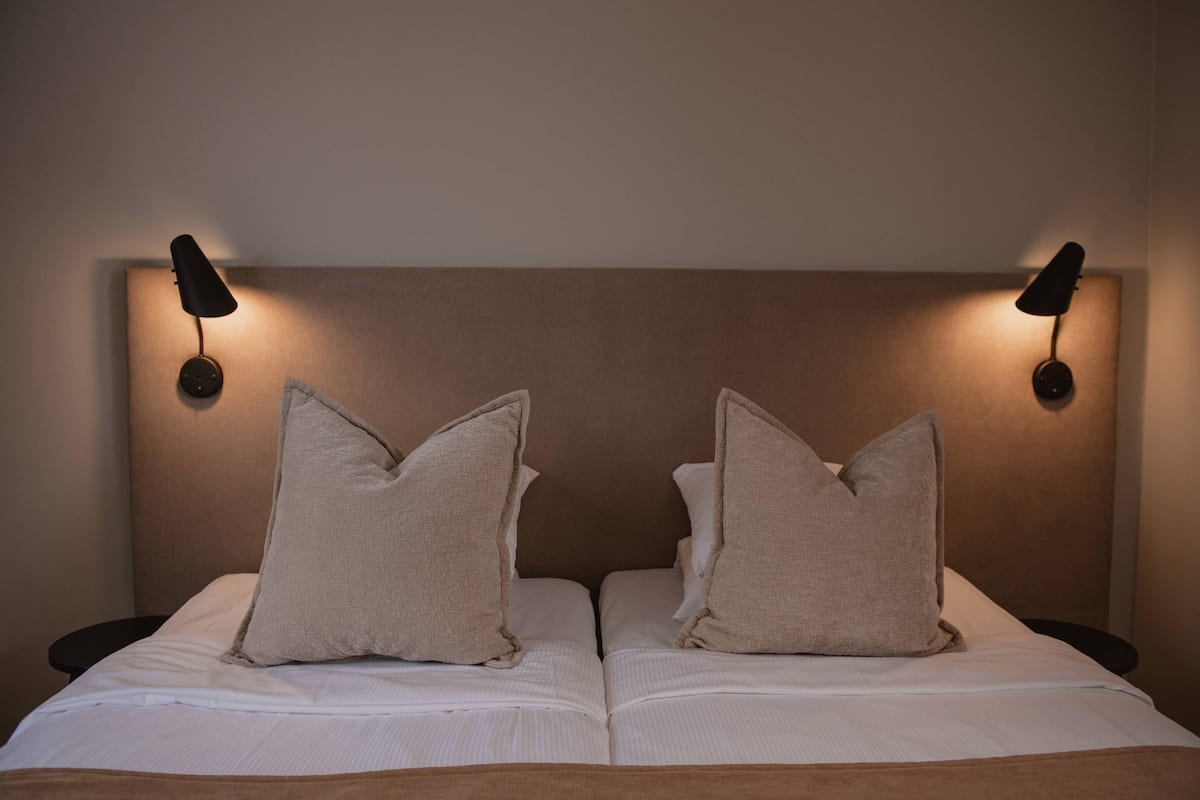 A double bed with two pillows, a headboard, and two wall-mounted lamps.