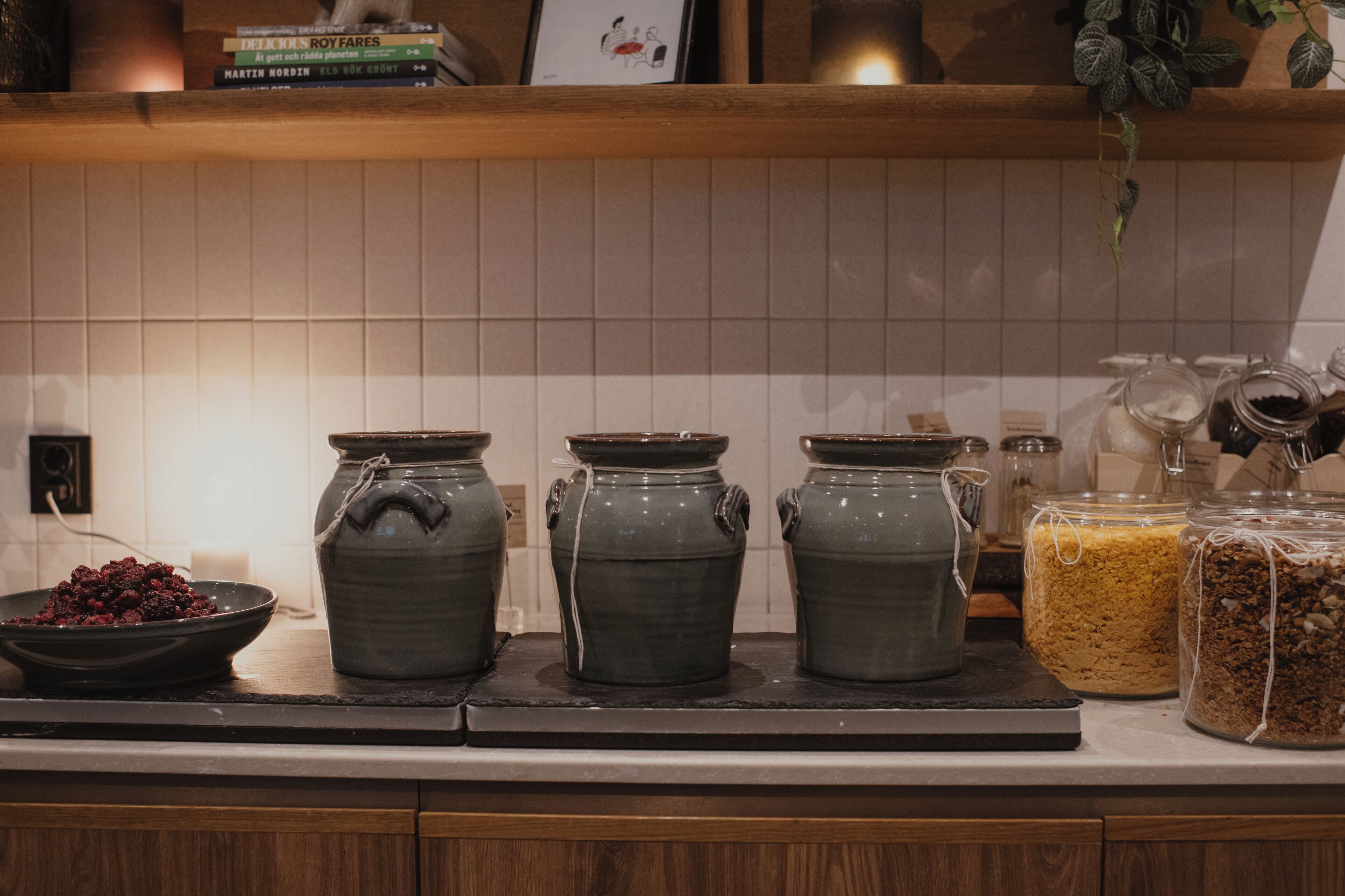 A kitchen counter with three ceramic pots, a bowl of berries, and two glass jars with food items.