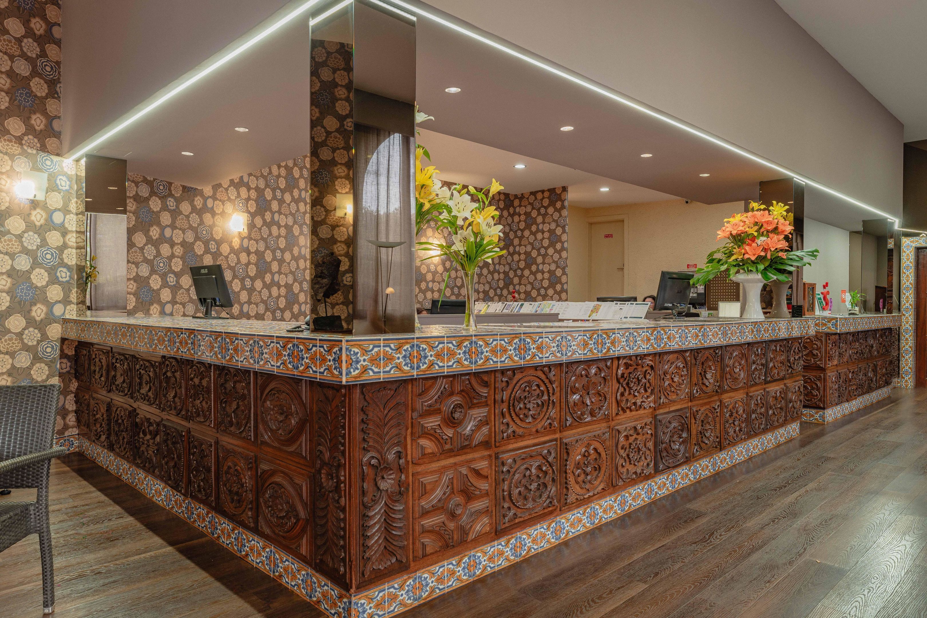 A reception area with a wooden counter, patterned walls, and a large vase of flowers.