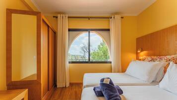A hotel room with two beds, a large arched window, wooden flooring, and a wooden headboard.