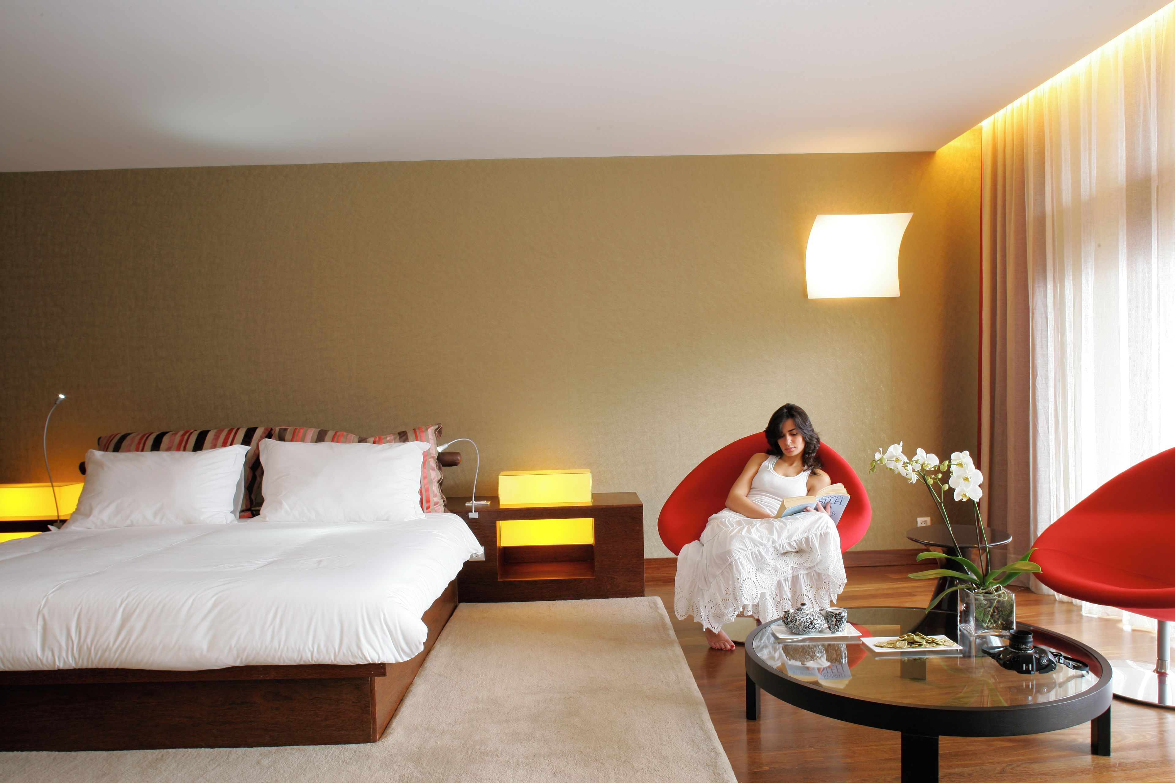 Ein Hotelzimmer mit einem großen Bett, einem roten Sessel, einem kleinen Tisch mit Blumenvase und einer Lampe.