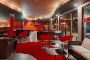 A modern lounge area with red chairs, wicker sofas, and a red carpet.