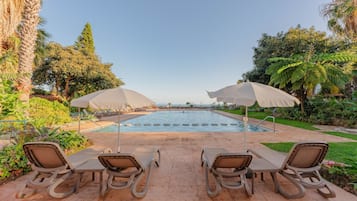 A pool area with lounge chairs and umbrellas, surrounded by greenery and trees.