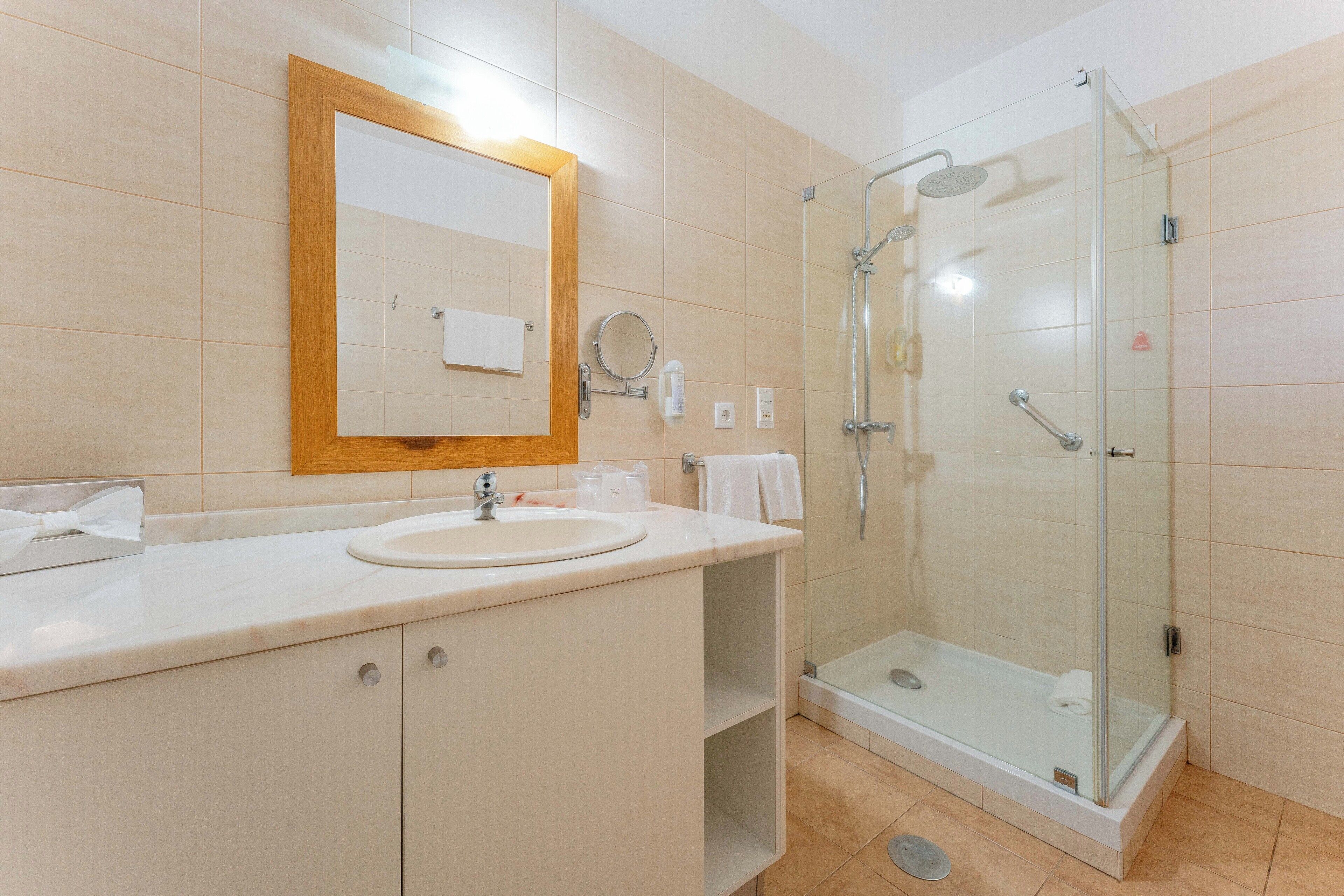 Un baño moderno con ducha de vidrio, un lavamanos con espejo y un espejo con marco de madera en la pared.