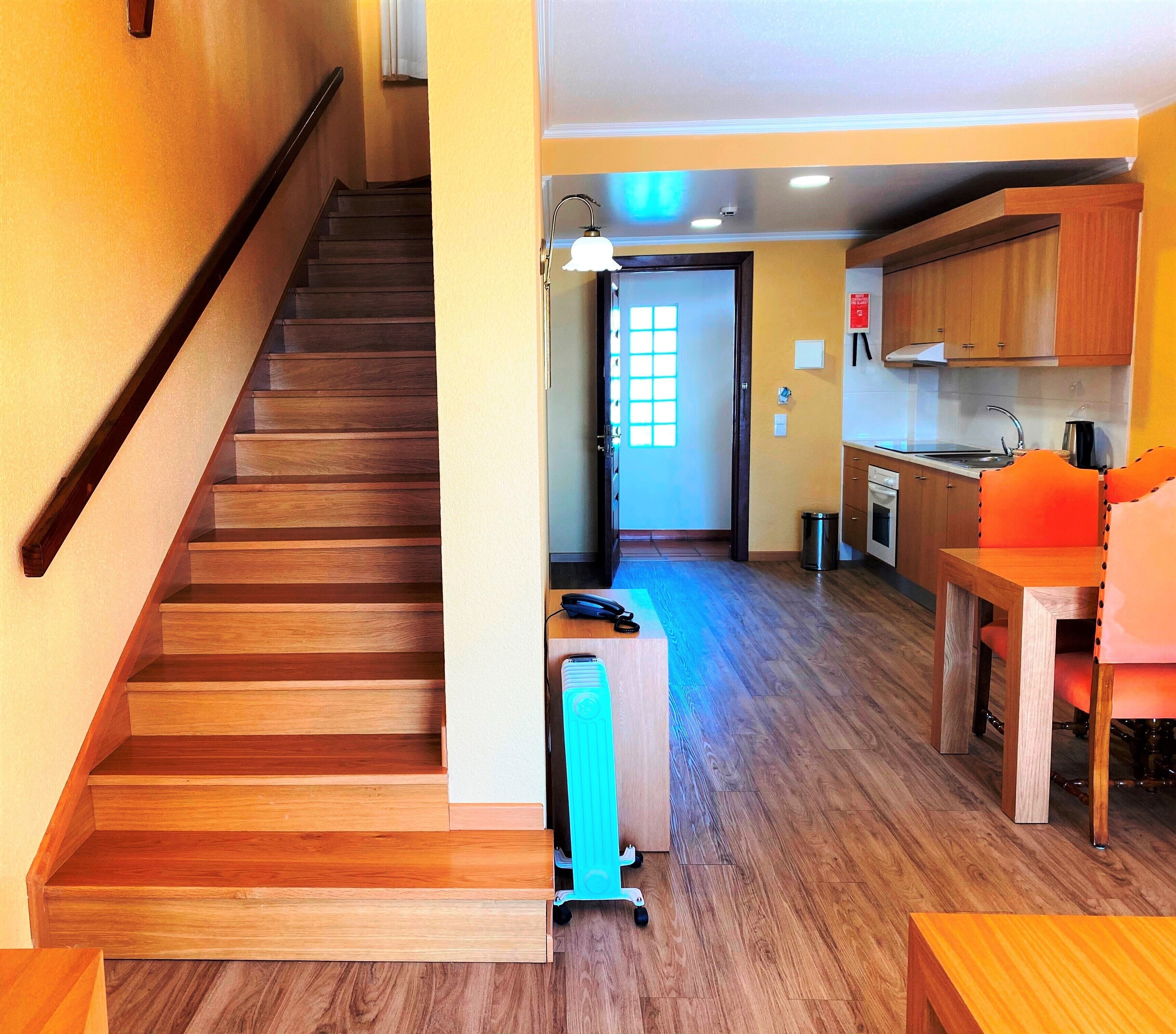 A wooden staircase leading to a kitchen area with wooden cabinets, a sink, and a dining table with chairs.