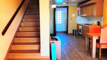 A wooden staircase leading to a kitchen area with wooden cabinets, a sink, and a dining table with chairs.