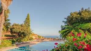 Una piscina con sillas de descanso, un edificio con techo curvo y vista al mar.