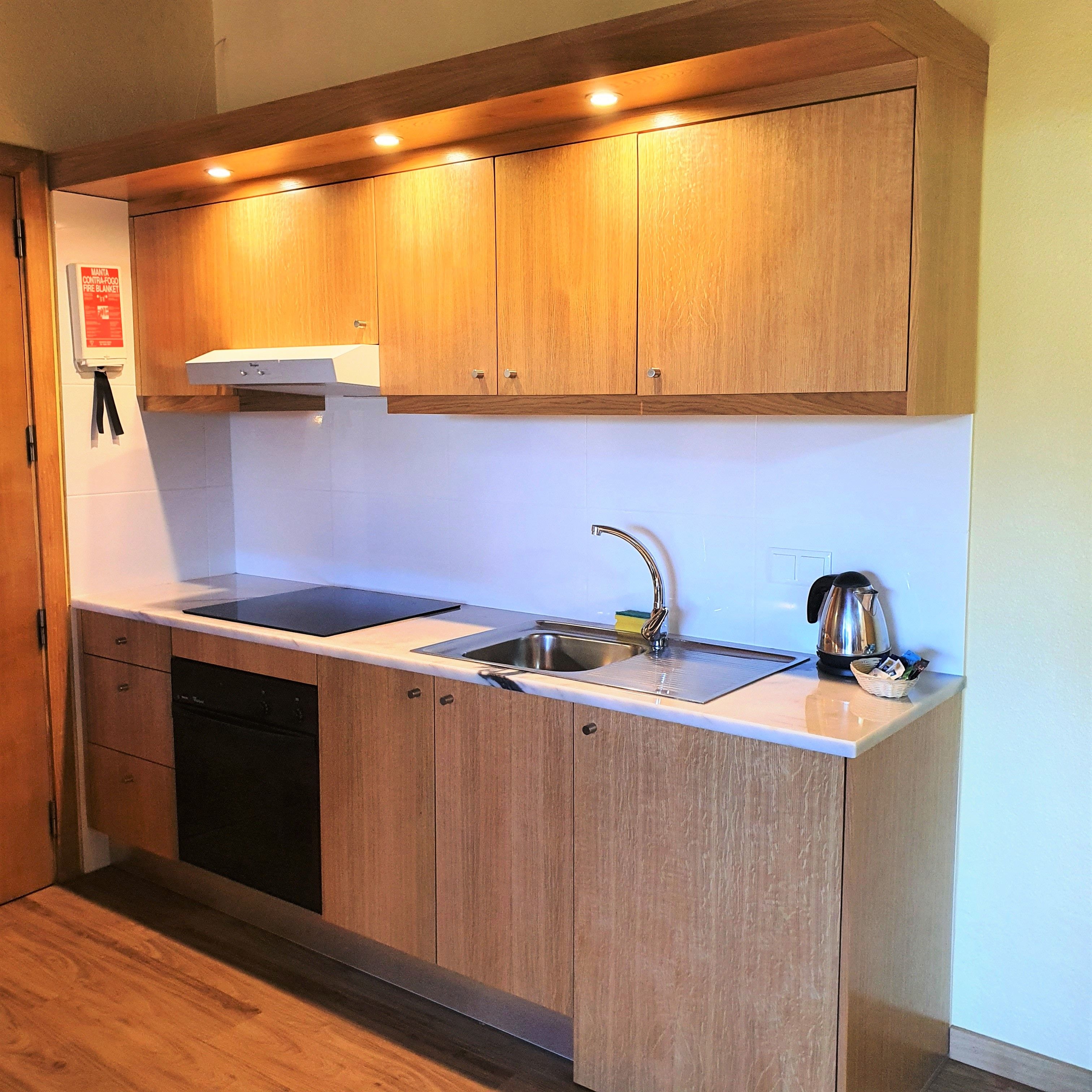 Una cocina moderna con armarios de madera, un lavamanos de acero inoxidable y una tetera sobre la encimera.