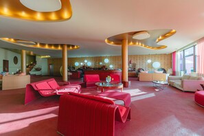 A modern hotel lobby with red seating, a reception desk, and a large window with curtains. - Quinta Splendida Wellness & Botanical Garden (Santa Cruz)