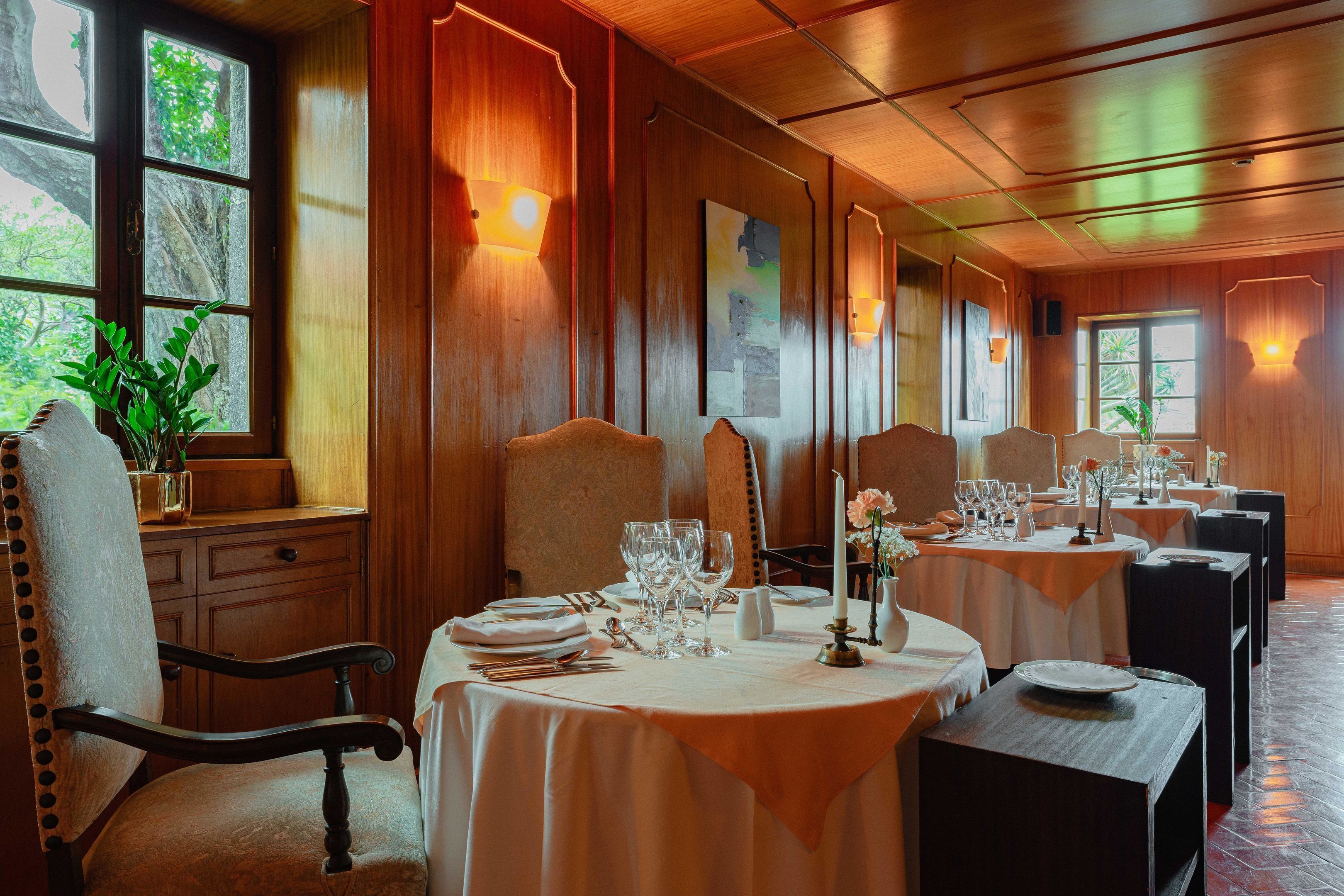 Comedor con paneles de madera, varias mesas dispuestas con manteles blancos y centros de mesa con velas.