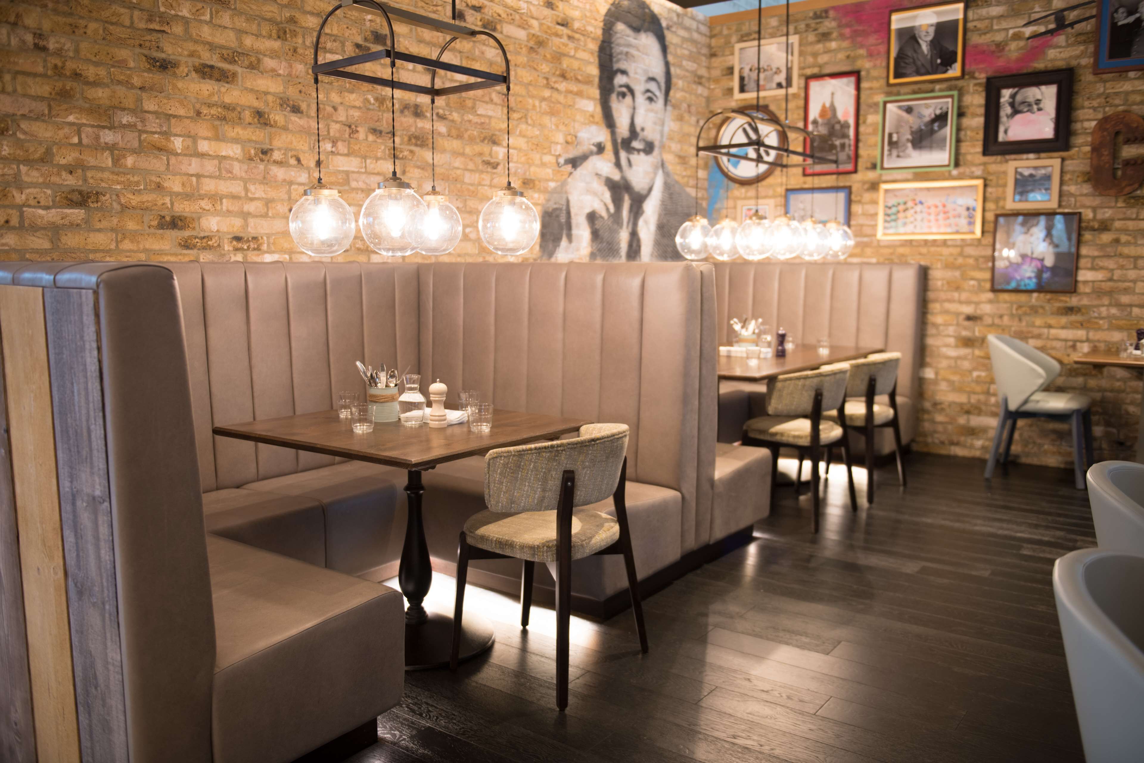 A restaurant with booth seating, pendant lighting, and a brick wall with framed pictures.