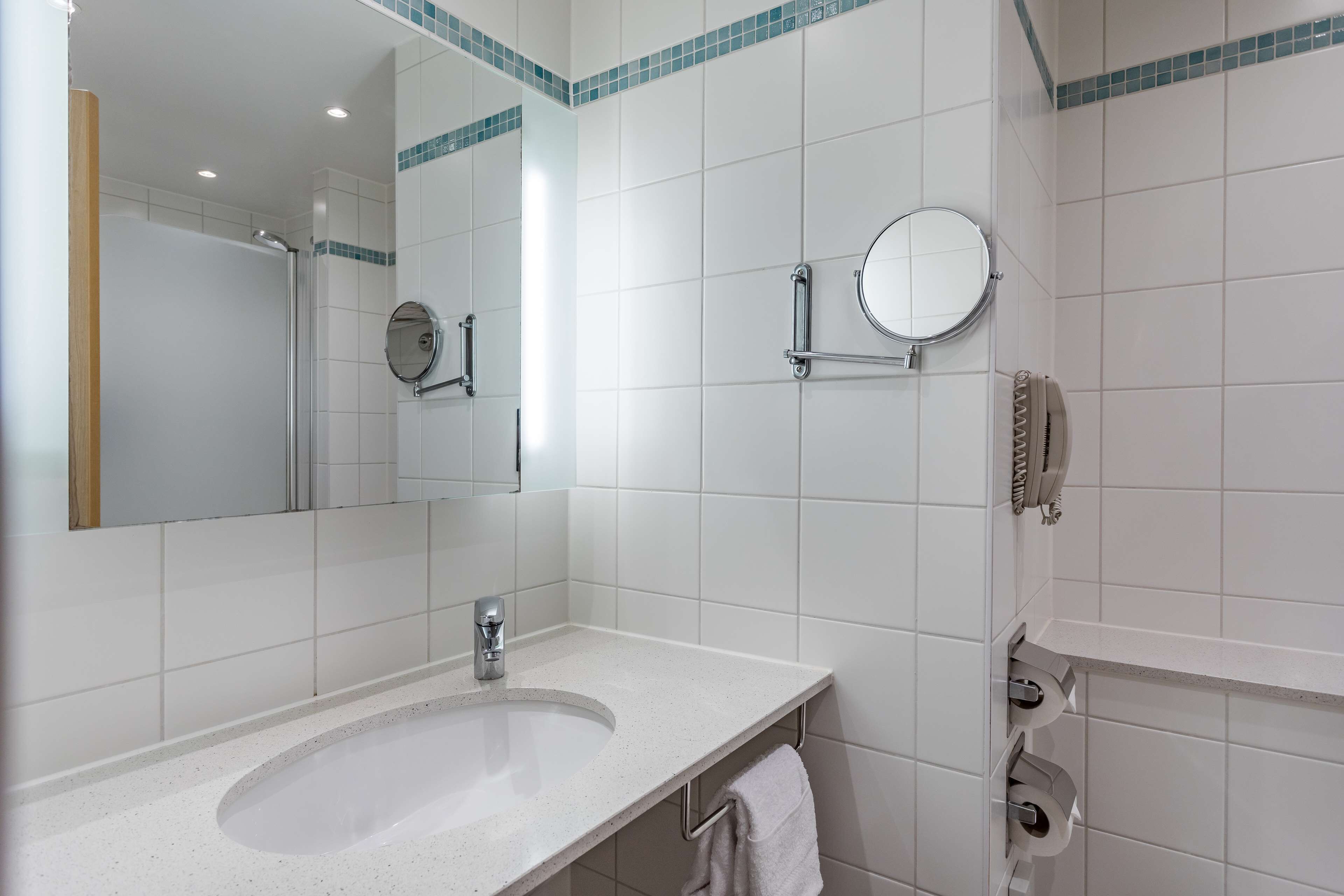 A bathroom with a sink, mirror, towel rack, and a shower area.
