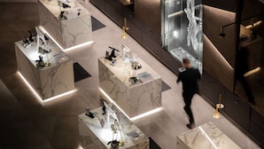 Un moderno vestíbulo de hotel con mostradores de recepción de mármol, una gran escultura de vidrio y un hombre caminando.