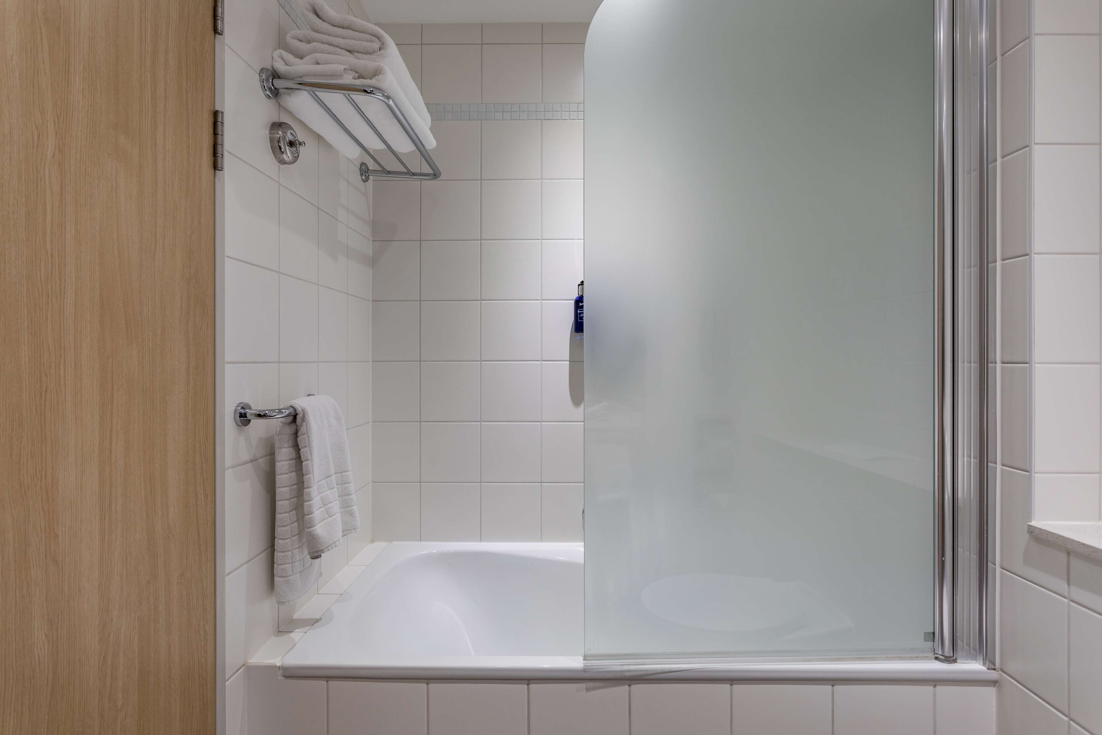 A modern bathroom with a glass shower enclosure, a white bathtub, and a wooden door.