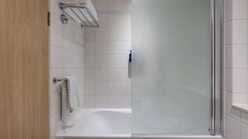 A modern bathroom with a glass shower enclosure, a white bathtub, and a wooden door.