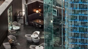 Een modern interieur met een zithoek met ronde tafels en comfortabele stoelen, een glazen vitrine met diverse objecten, en een trap met donkerhouten beleding.