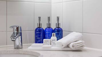 Une salle de bain avec un lavabo moderne, trois flacons bleus de gel douche Radisson, un flacon blanc de lotion et une serviette blanche soigneusement pliée posée sur le comptoir.