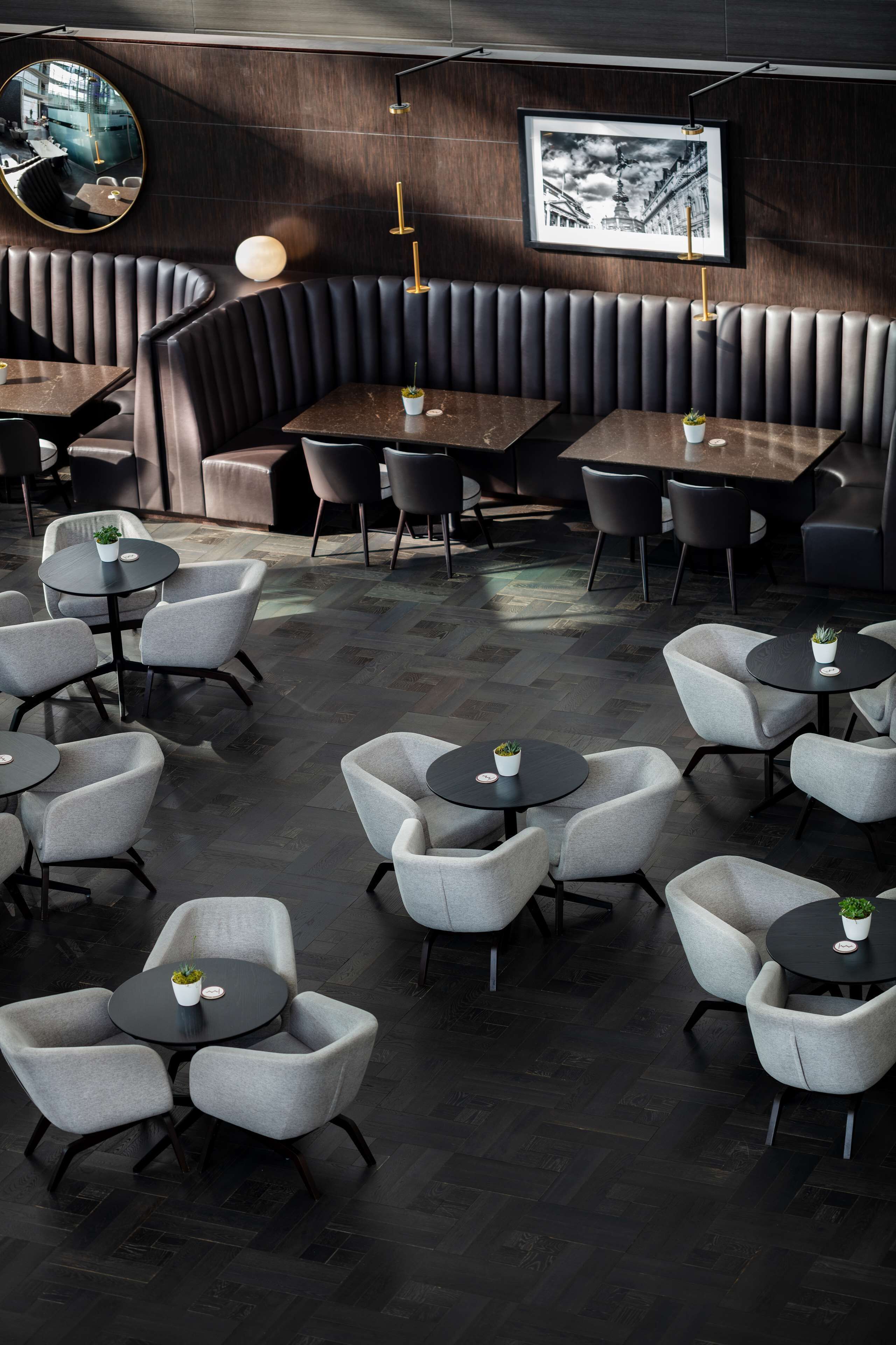 Un intérieur de restaurant moderne avec des lambris en bois foncé, un espace de sièges en forme de banquette incurvée, ainsi que plusieurs tables et chaises.