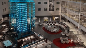 Un moderno vestíbulo de hotel con un atrio central, una zona de bar y diferentes disposiciones de asientos.