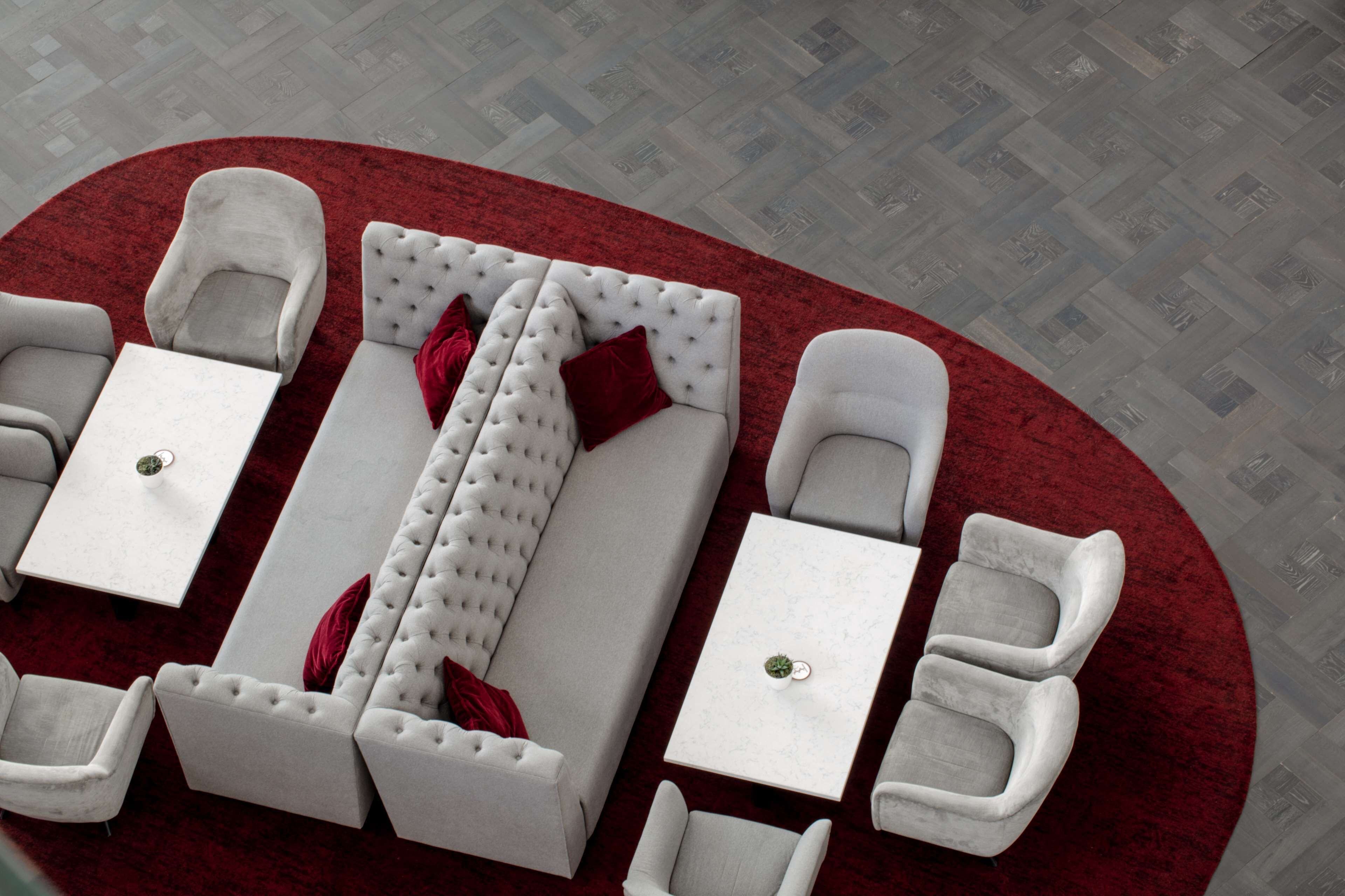 Una habitación de hotel moderna con alfombra roja, sofás blancos y sillones a juego.