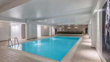 An indoor swimming pool with clear blue water, tiled floor, and a modern design.
