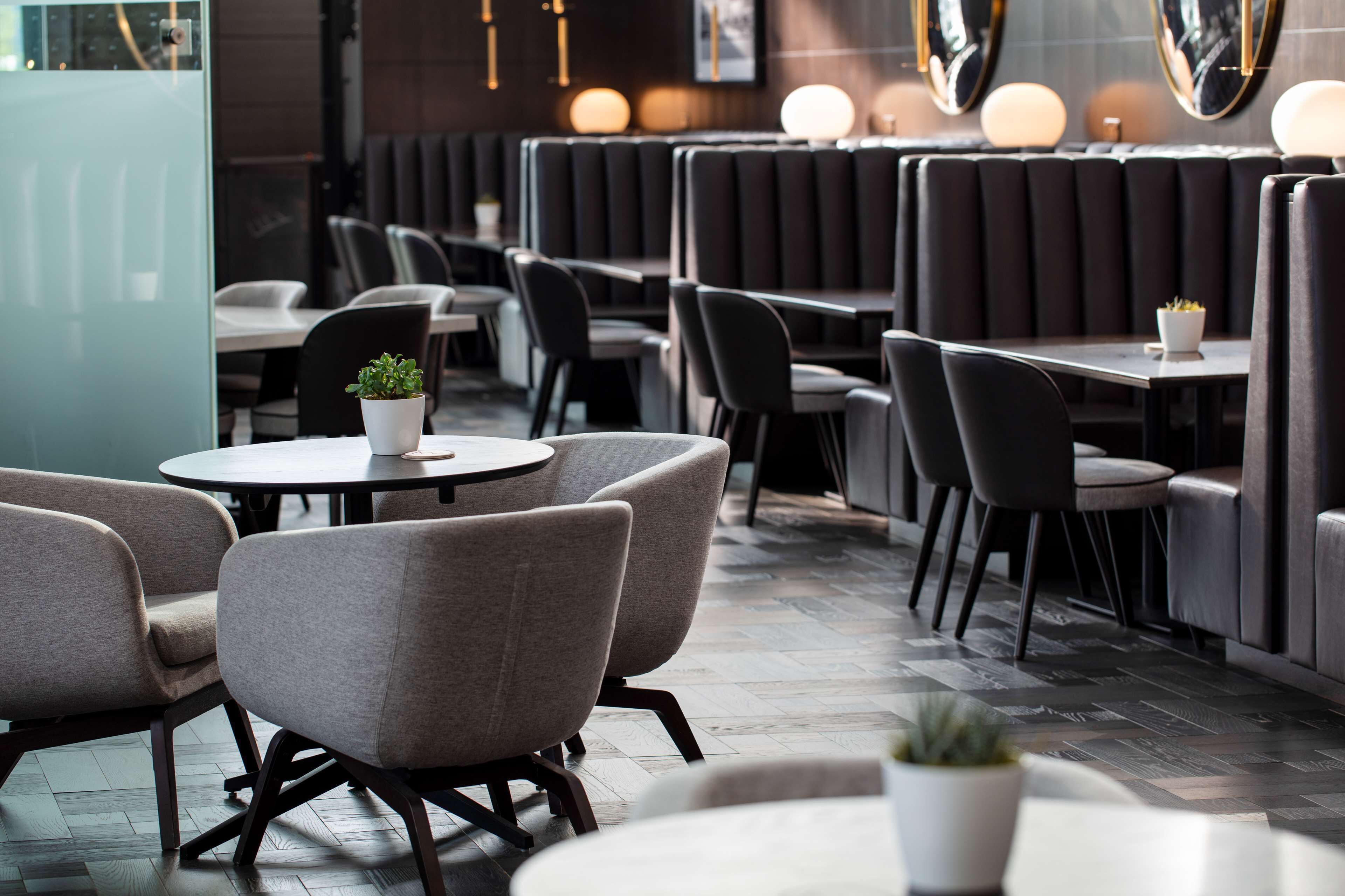 A restaurant interior with booth seating, round tables, and potted plants.