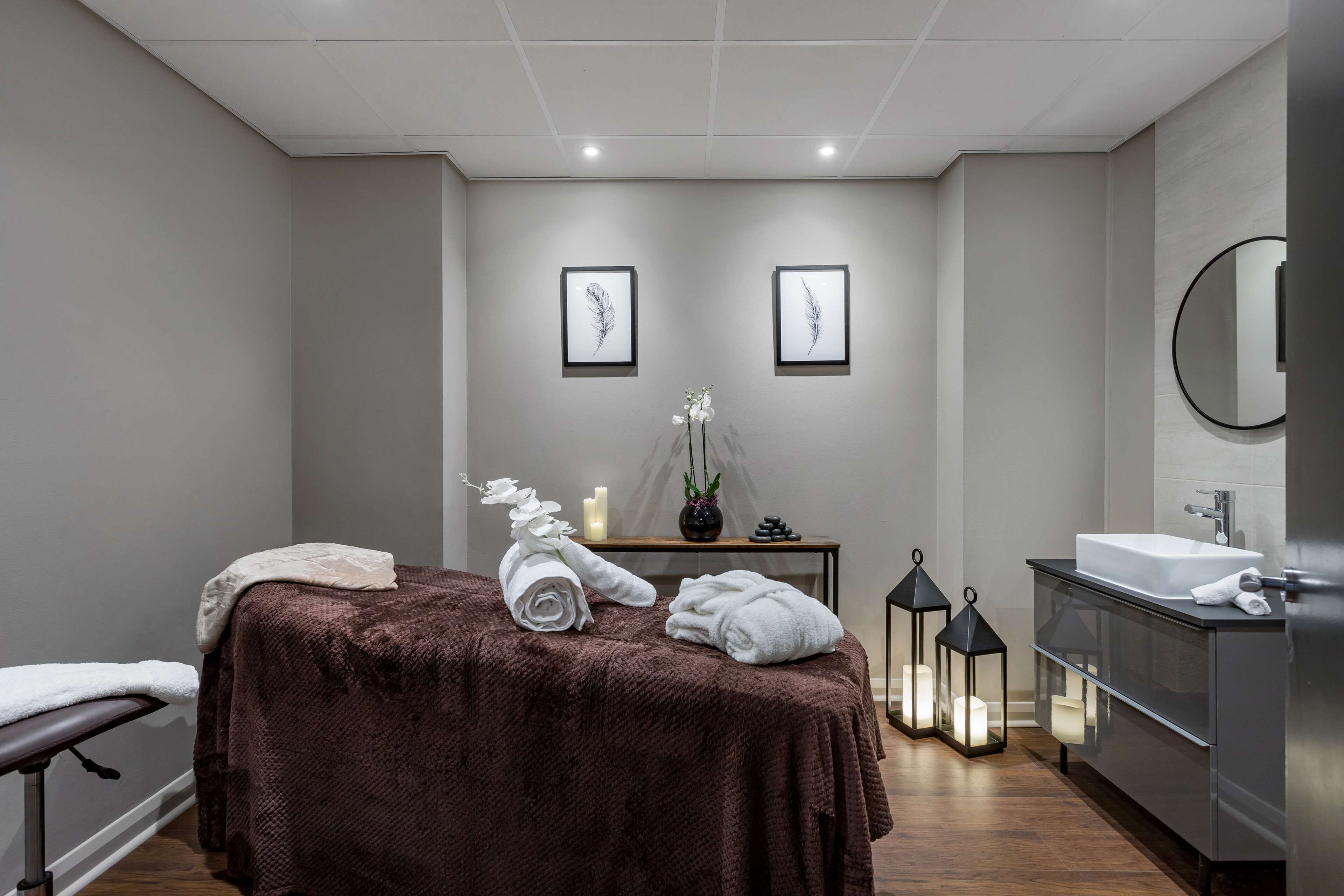 A modern spa room with a massage table, candles, and a mirror.