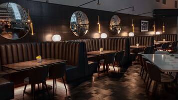Un interior de restaurante moderno con asientos de cuero, mesas redondas y paredes espejadas que reflejan el paisaje urbano.