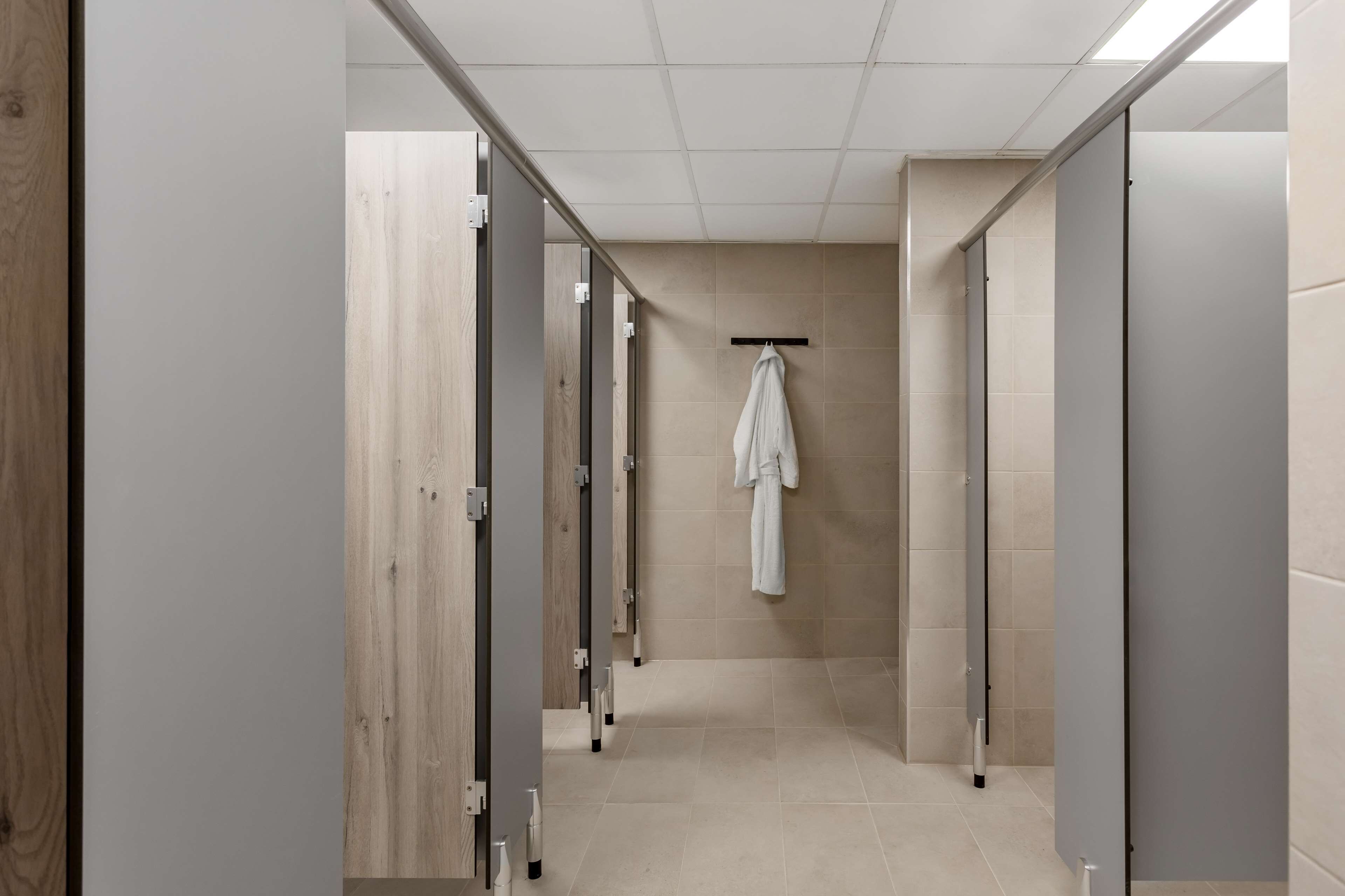 A corridor with multiple stalls, each with a wooden door and a towel hanging on a rack.