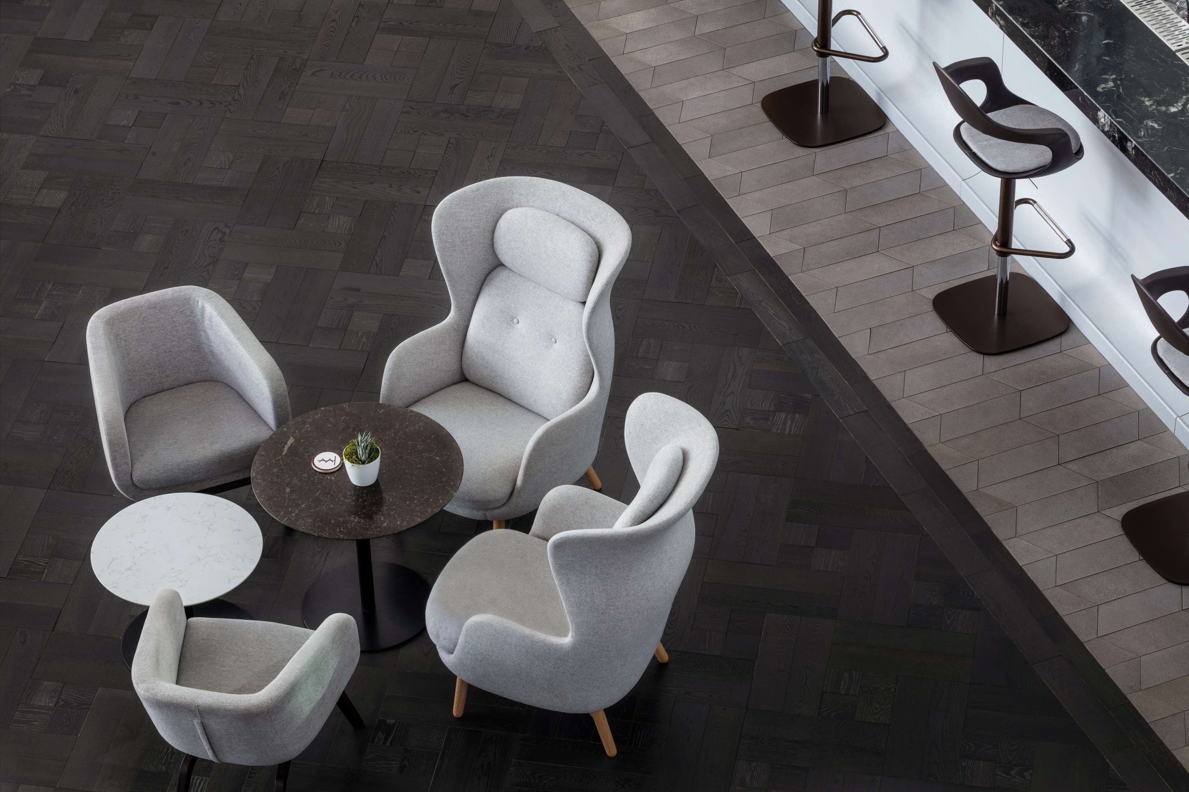 A modern lounge area with grey upholstered chairs and a round table, featuring a small potted plant.