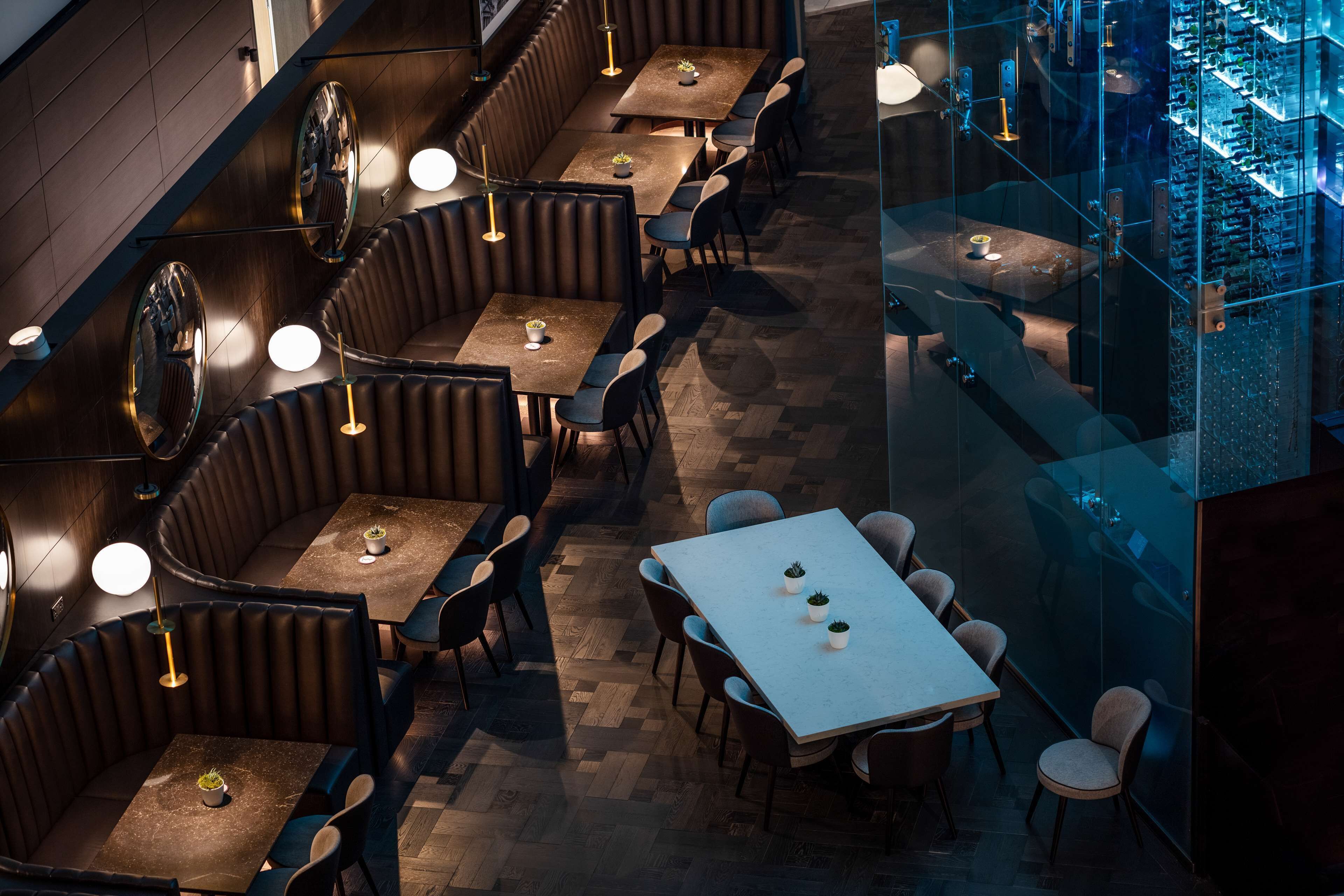 A restaurant with booths and tables, wooden flooring, and pendant lighting.