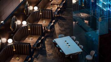 A restaurant with booths and tables, wooden flooring, and pendant lighting.