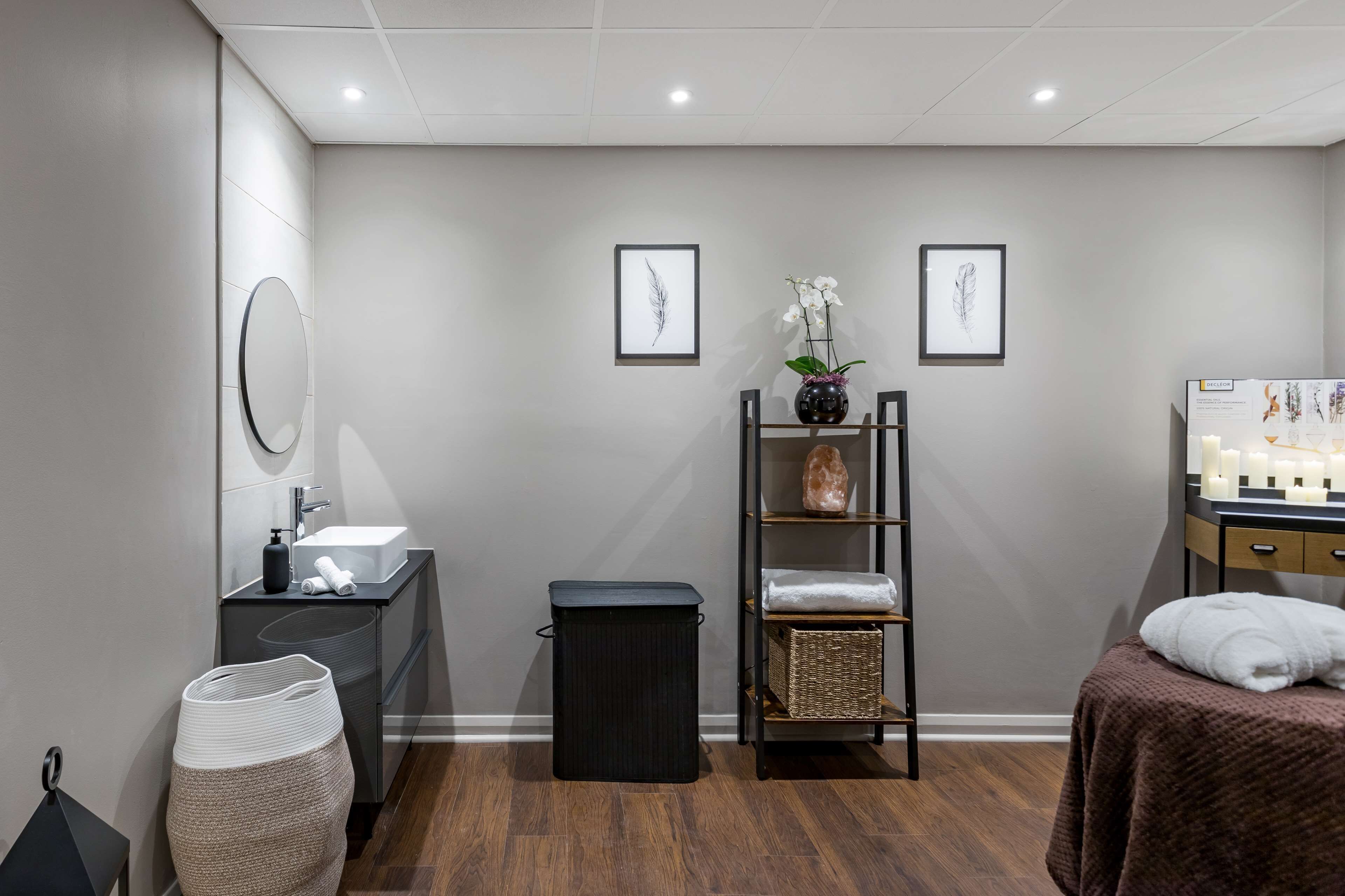A modern bathroom with a sink, mirror, and a shelf with towels and a vase of flowers.