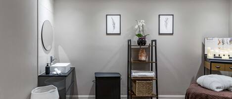 A modern bathroom with a sink, mirror, and a shelf with towels and a vase of flowers.