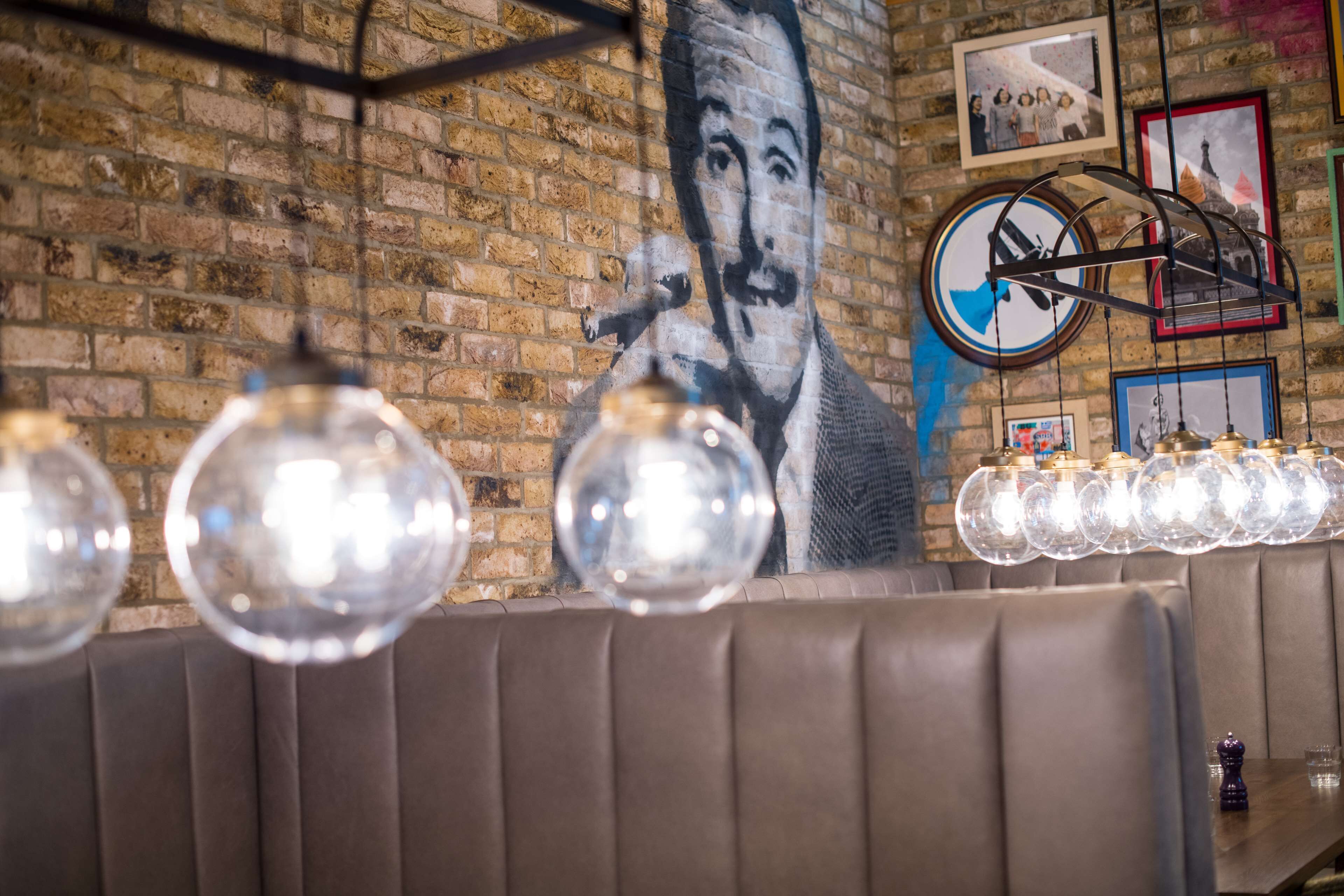 Interior de restaurante com paredes de tijolo, um mural e uma fileira de globos iluminados.