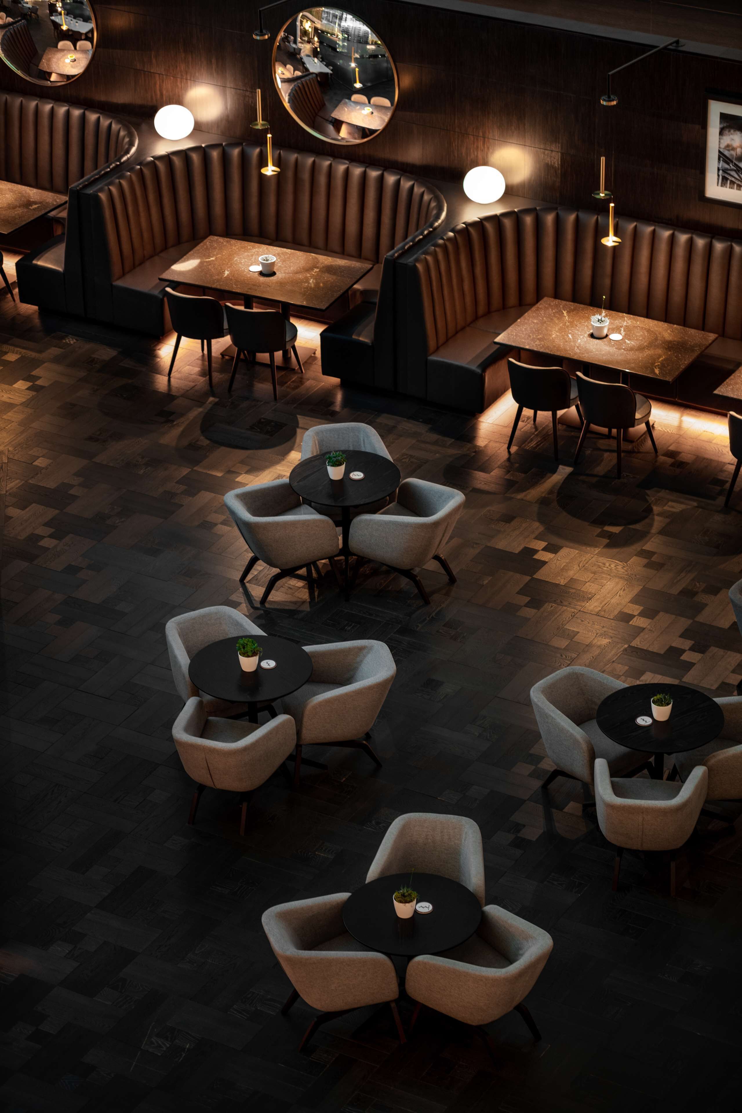 A restaurant with booth seating and round tables, featuring a herringbone floor pattern and pendant lighting.