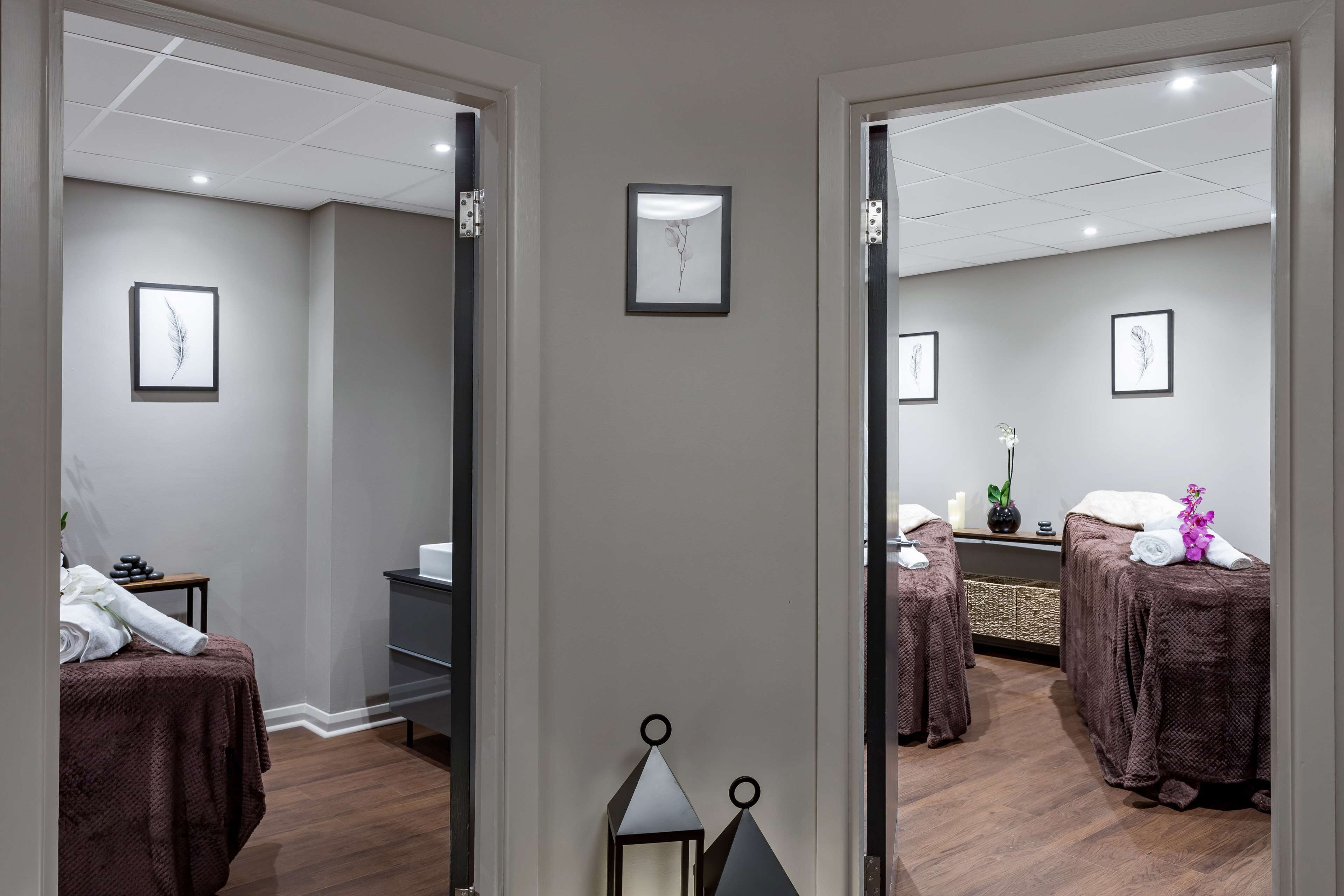 Habitación de spa con una cama, una mesa de masaje y una estantería en la pared con un jarrón y una planta.