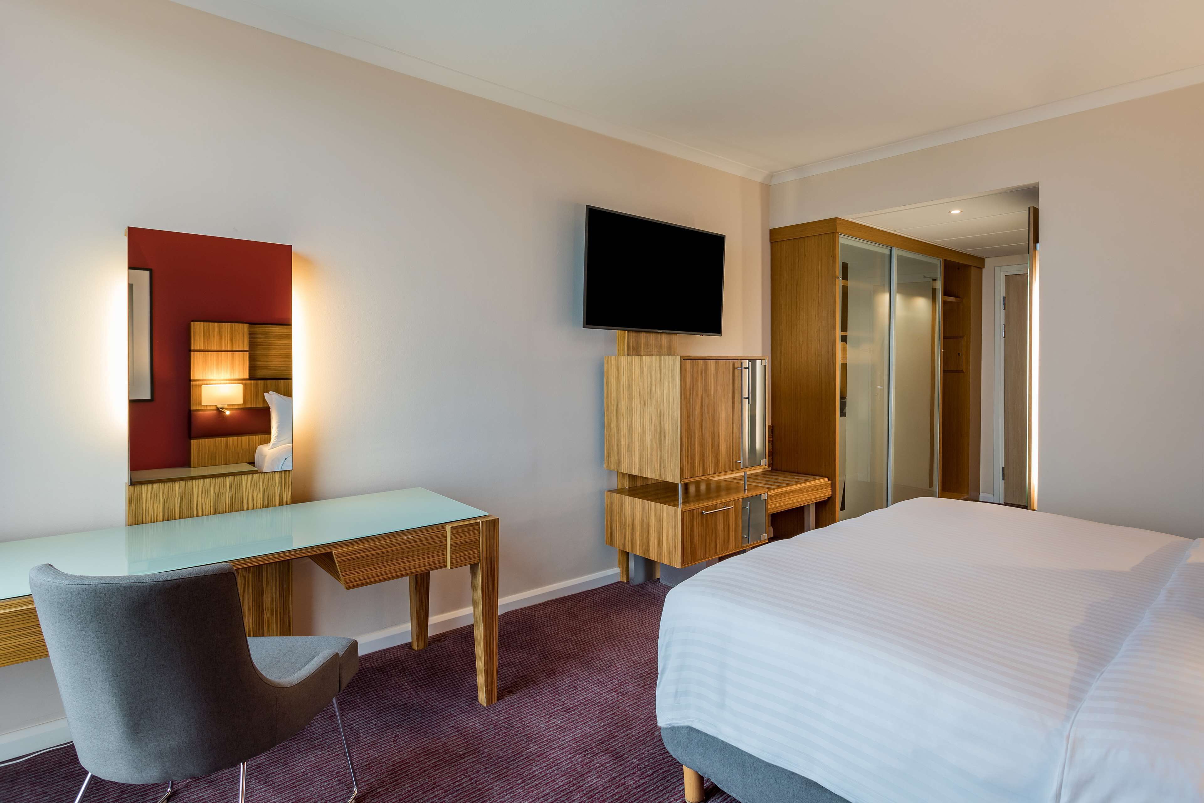 Una habitación de hotel con cama, escritorio, silla, televisor y armario.